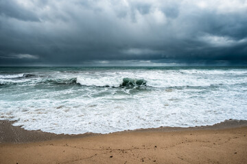 Rough seas crash onto the beach at Algajola in the Balagne region of Corsica with dark clouds and...