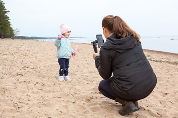 Mother taking picture with her small daughter playing soap bubbles on empty sandy beach