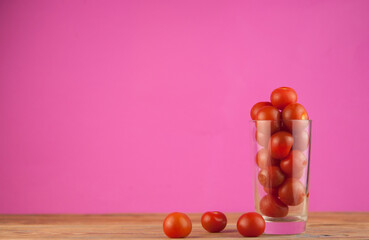 small red cherry tomatoes in a clear glass cup on a wood table background. red vegetables