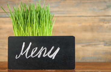 Menu written with chalk on aged blackboard over spring grass background. Grass over wood. Nature background with grass and wood