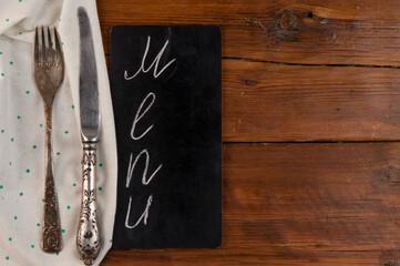 Menu written with chalk on aged blackboard with kitchen utinensil on wooden table.
