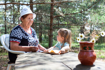 Little girl asking to read the book her grandma, senior and young family members, summer