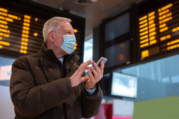 Masked businessman using his smartphone while waiting for the train, covid and coronavirus mobility concept