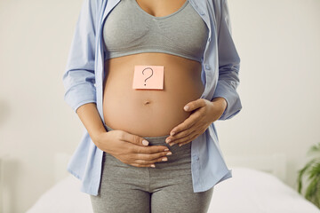 Beautiful naked belly of pregnant woman on which is pasted paper sticker with question mark....