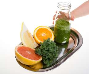 Child's hand lifting a bottle with citrus and cale juice. Kid hand pointing to healthy smoothie jar and vegetables and fruit on a plate