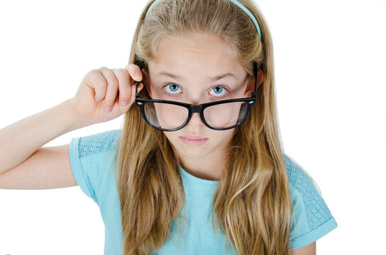 Close-up portrait of beautiful serious focused blond girl wearing glasses holding frame and looking at camera over the top of specs. Isolated on white background 