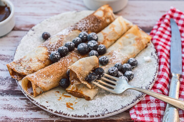 Dish with delicious homemade pancakes or crepes filled with dulce de leche. Fork with a bite and some spiked blueberries. high view