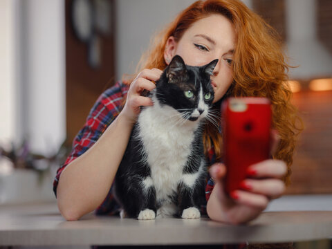 portrait of a beautiful cheerful young woman with a black and white cat in her arms at home. Animals and lifestyle concept. taking selfie on smartphone with pet