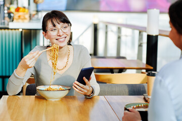 Portrait of smiling young woman enjoying delicious Asian noodle in cafe and eating wok with...