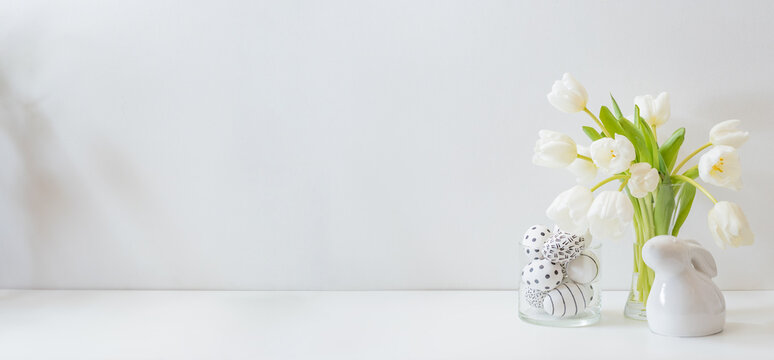 White spring tulips in a vase, easter eggs on a white table. Mock up for displaying works