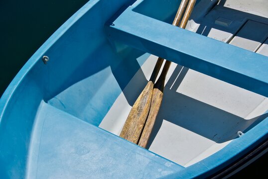 Blue rowing boat with shadow image and two oars laying under seat board.