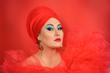 Portrait of a beautiful woman in oriental style. A girl with bright professional makeup, stylish jewelry, a red turban on her head. A pretty lady with a cloth tied on her head, red lips and makeup