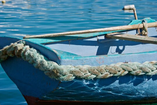 Detail of a small blue Maltese fishing boat with braided rope and oars.
