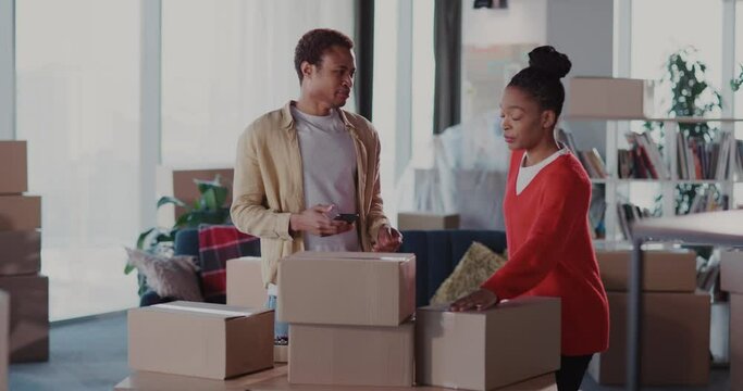 Joyful excited couple of married afro-american man with woman counting cardboard boxes with furniture in empty old apartment. Moving house.