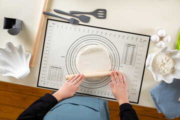 Naklejka premium Top view of the process of rolling wheat dough on a kitchen mat.