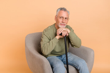 Photo of optimistic old grey hairdo man sit with stick look promo wear pullover jeans isolated on beige background