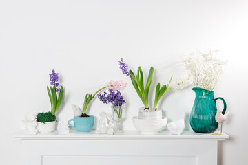 White hyacinth in a large porcelain bowl, figurines of hares and a bird, are on the fireplace against the white wall. Layout. Spring concept