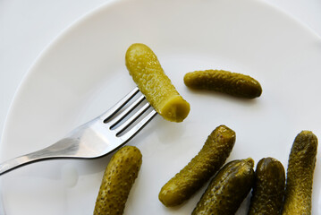 Green pickles on a white plate and a fork