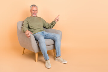 Full length photo of nice old grey hairdo man sit index promo wear pullover jeans footwear isolated on beige background