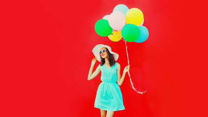 Happy young woman with bunch of colorful balloons on red background