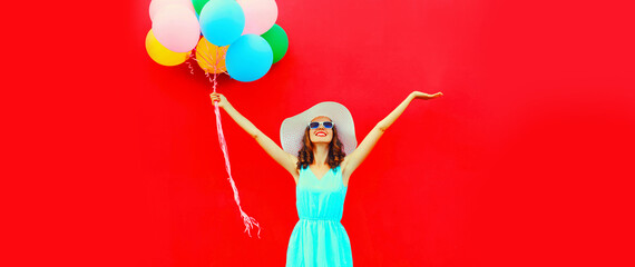 Happy joyful woman with bunch of colorful balloons raising her hands up on red background