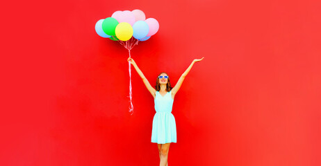 Happy joyful woman with bunch of colorful balloons raising her hands up on red background, blank copy space for advertising text