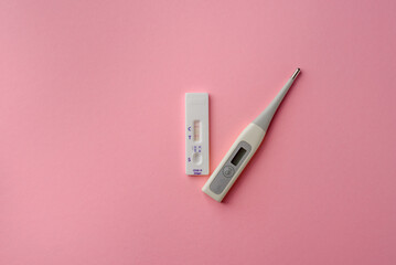 Express test for covid-19 with a positive result and a thermometer on a pink background. Coronavirus self-test kit