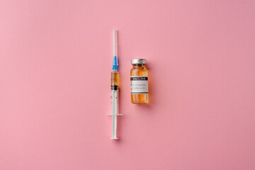 Syringe and ampoule with vaccine against coronavirus covid-19, pink background, flat lay
