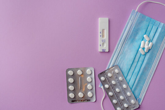 Medical set of pills and vitamins, medical mask, covid-19 self test. Purple background, flat lay, copy space