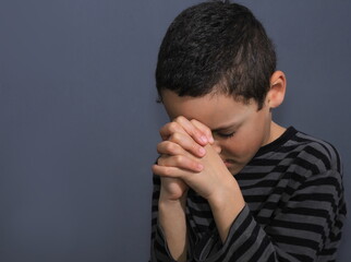 little boy praying to God with eyes closed with grey background stock photo
