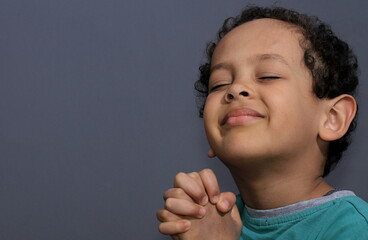 little boy praying to God with eyes closed with grey background stock photo