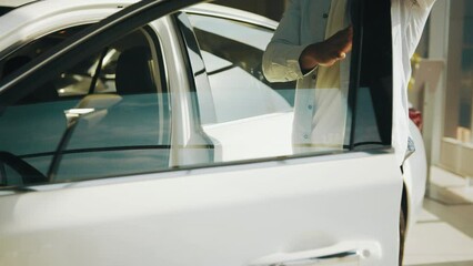 Handsome man in casual wear feeling satisfaction from expensive purchase at auto salon. Buying car. The buyer opens the car door at the dealer. African man examining new car at modern showroom.