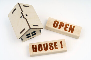 On a white surface, a wooden toy house and blocks with the inscription - OPEN HOUSE