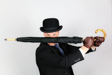 Portrait of British Gentleman in Dark Suit and Bowler Hat Holding Umbrella in Action Pose. Concept...