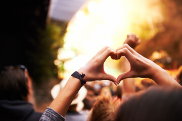 Appreciating the art of performance. A young woman gesturing a heart towards the stage at a music festival.