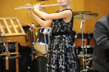 A girl student of a music school plays a flute concert standing on the stage in an elegant dress with raised hands holding an instrument real photo of a young musician during a performance