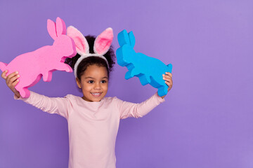 Portrait of attractive cheerful pre-teen girl holding bunnies playing toys isolated over bright purple violet color background