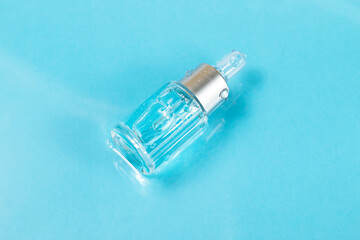 Bottle serum or cosmetic oil in clean transparent water with sunlight on blue background, flat lay, top view, copy space. Cosmetic spa medical skin care concept.