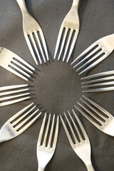 Cìrculo de tenedores de cocina de metal brillantes de cuatro dientes para comidas varias, forman un bello diseño abstracto con fondo gris