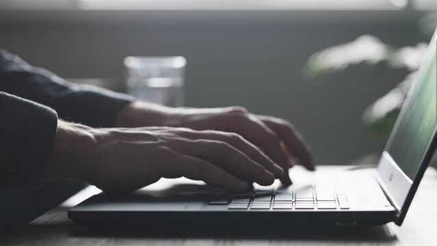 An unrecognizable man is typing very quickly on a laptop keyboard. High-speed printing of text and messages.