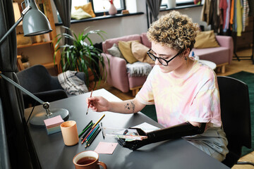 Girl in eyeglasses with prosthetic arm enjoying painting at table in living room - obrazy, fototapety, plakaty