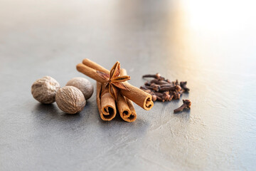 brown cinnamon sticks on which star anise lies, and around them nutmeg and cloves isolated on a gray background. Front view