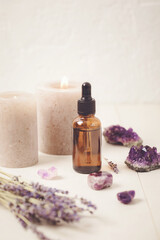 Fototapeta na wymiar Glass bottle of Lavender essential oil with lavender flowers and candles and amethyst crystals. Meditation, zen, aromatherapy,spa massage concept