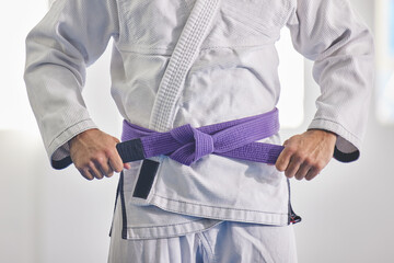 Im a purple belt. Cropped shot of an unrecognizable man tying a purple belt around hist waist while in full jiu jitsu gi.