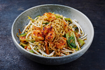 Modern style traditional stir-fried Thai phak kung with king prawns, vegetable and noodles served as close-up in a Nordic design bowl