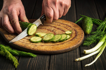 Cook cuts cucumber on a cutting board. Close-up of a chef hands while preparing a salad with fresh vegetables. Peasant cuisine