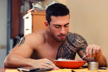 Handsome male bodybuilder eating rice at home