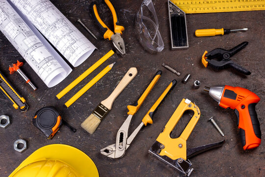 Working tools background. Project drawings roll, pencils, ruler, pliers, metal screws, handsaw and other accessories on black background. Repair and construction concept. Flat lay, top view image
