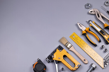 Working tools background. Screwdriver, tape measure, wrench, knife, pliers, pencils, ruler, pliers, metal screws, and other accessories on grey background. Repair and construction concept 