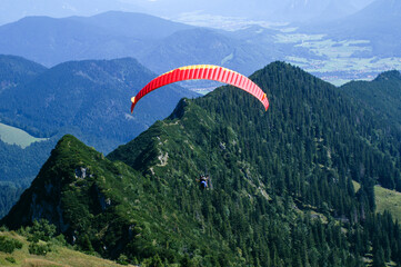 Paraglider tandem shortly after takeoff against wooded mountain ridge